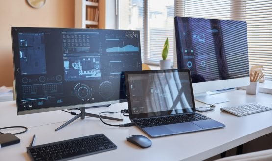 Row of three desktop computers with online graphic data on screens standing on workplace of IT engineer in office environment